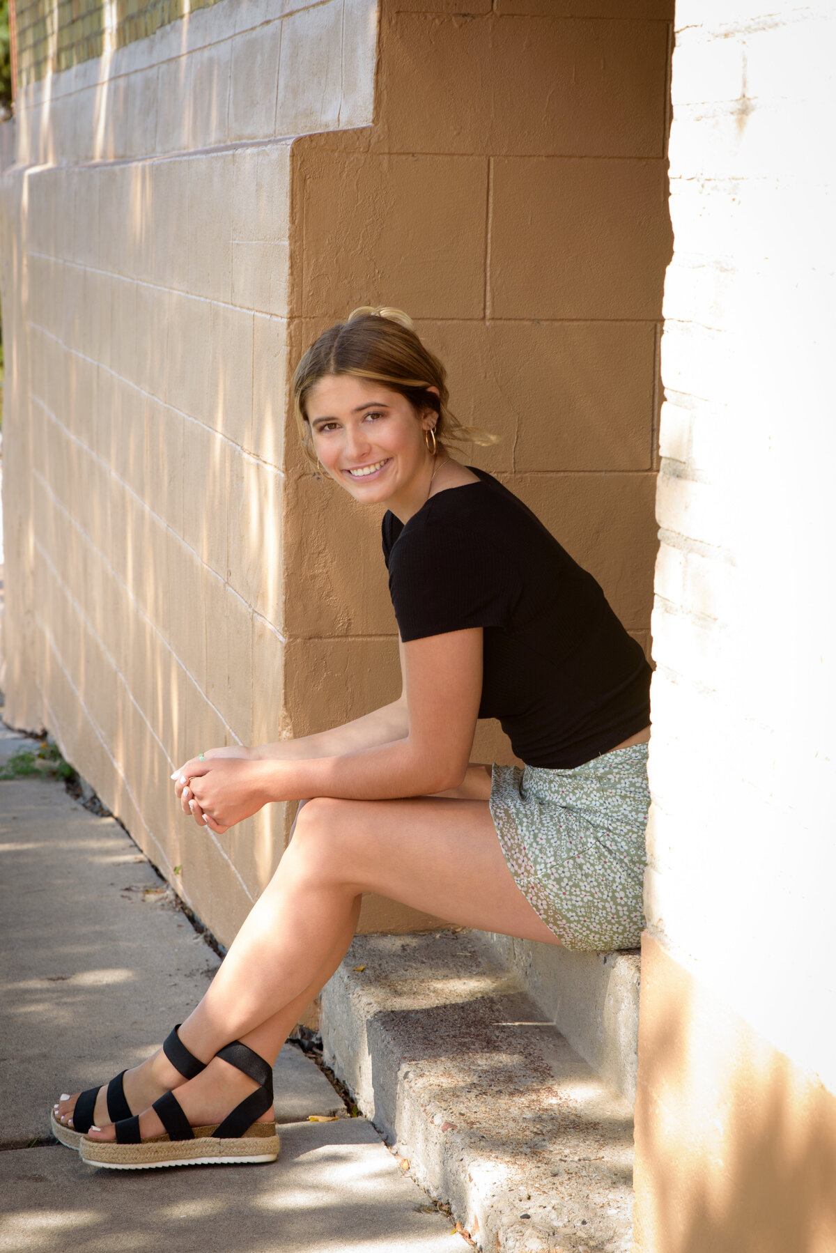 close up head shot of De Pere High School senior girl wearing a short green skirt and black shirt sitting on stairs in an urban setting near Voyager Park in downtown De Pere, Wisconsin