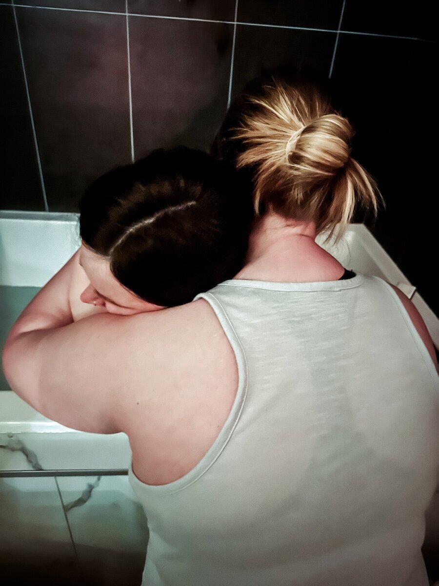 a pregnant woman laboring in the tub with support of her wife
