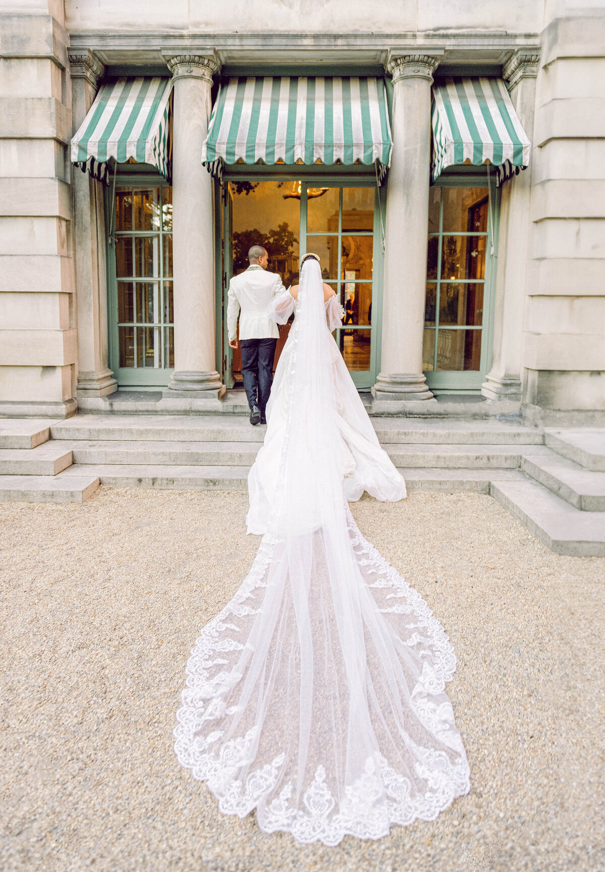 Bride in a flowing cathedral veil walking into Anderson House in Washington DC, hand in hand with her partner, captured by Mari Harsan Studios during a luxury wedding.