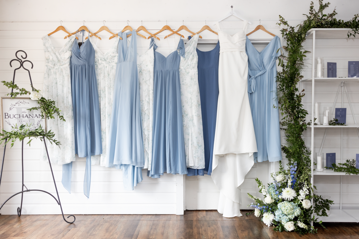 Spring wedding at WinMock at Kinderton, designed by Charming Carolina — bridesmaids’ dresses in shades of dusty blue and the bride’s wedding gown hanging in the hallway of the venue.