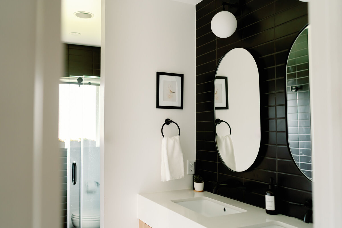 black subway tile horizontal stack behind sinks in bathroom with rounded rectangular mirrors