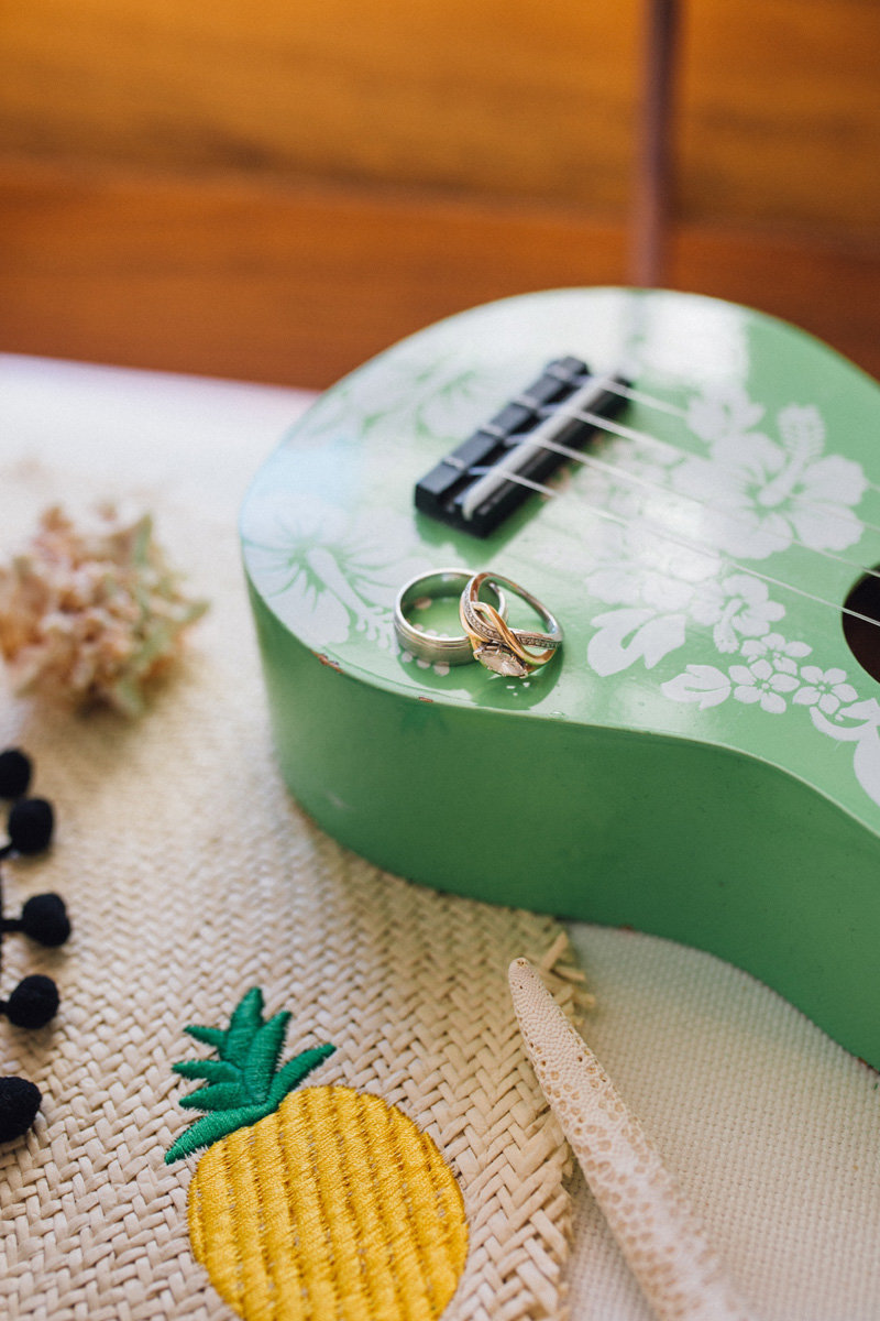 Wedding rings on a green ukelele by a straw hat with a pineapple