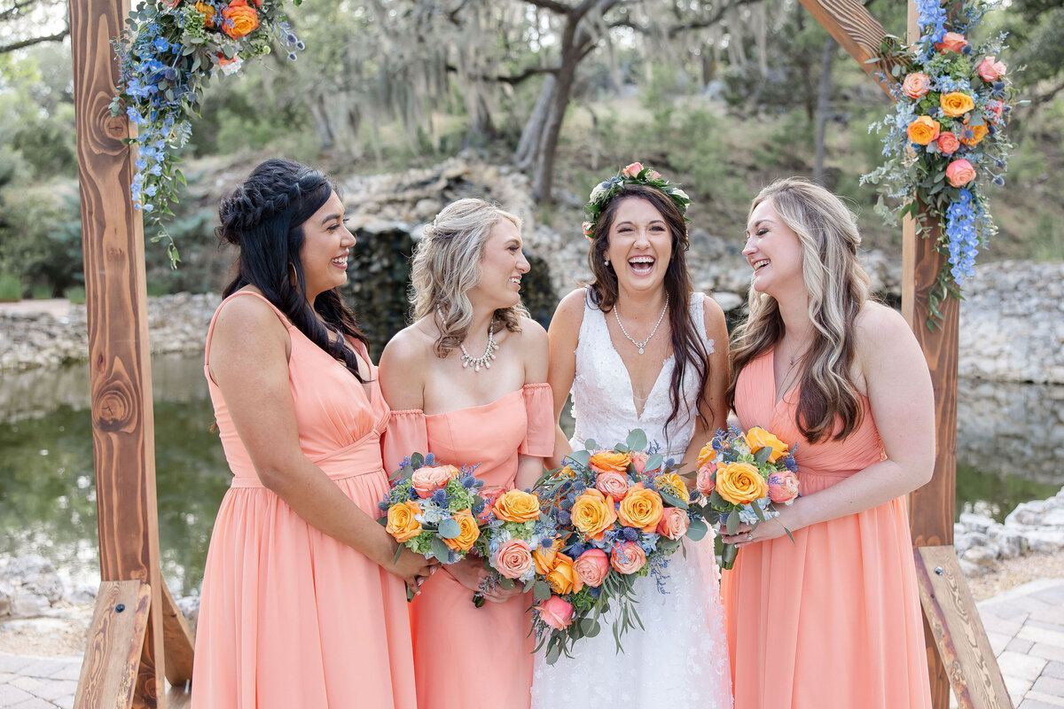 bridesmaids in peach dresses laugh together at Hayes Hollow at Hidden Falls wedding in Spring Branch Texas