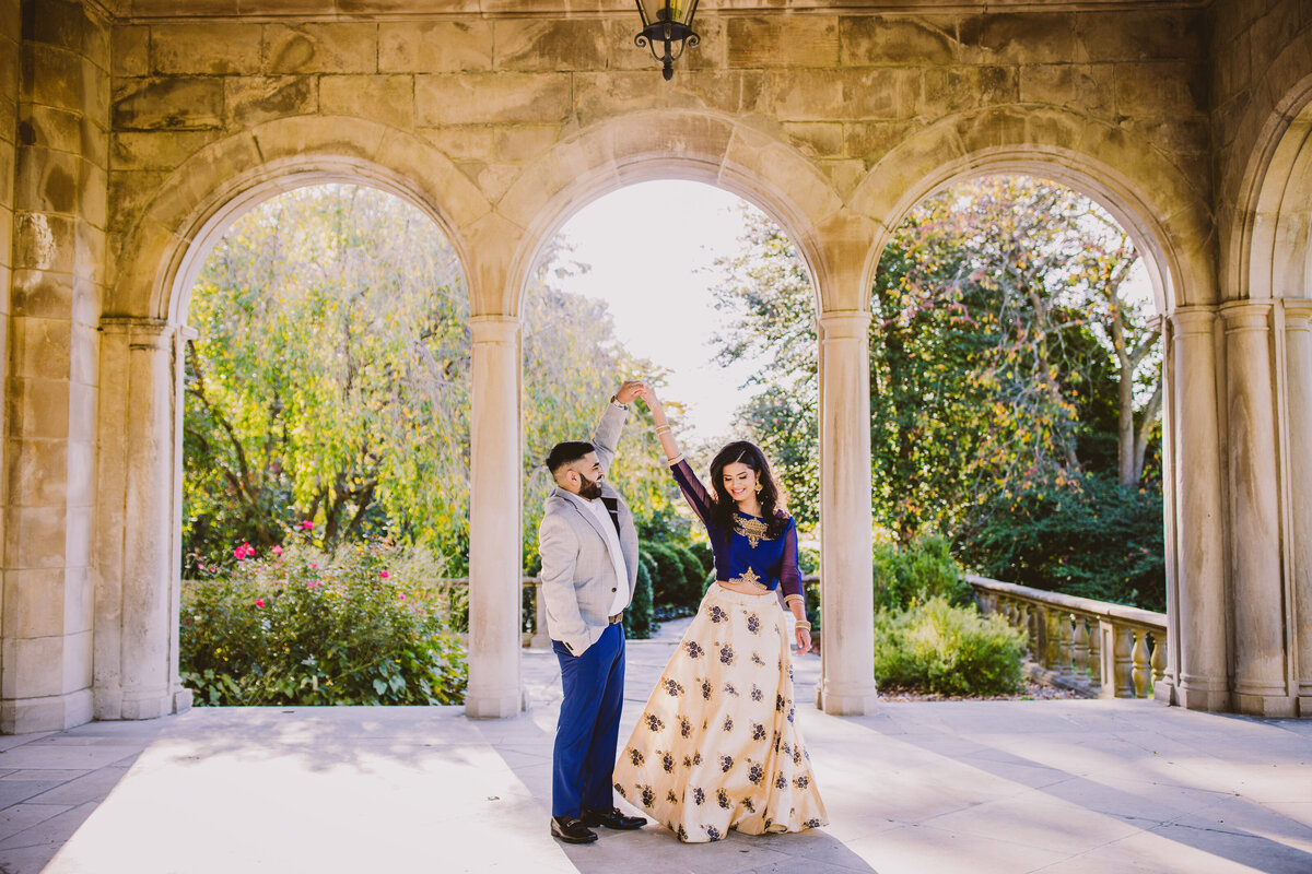 An engaged couple twirling in the canopy of a mansion under the arches at planting fields arboretum in oyster bay, ny