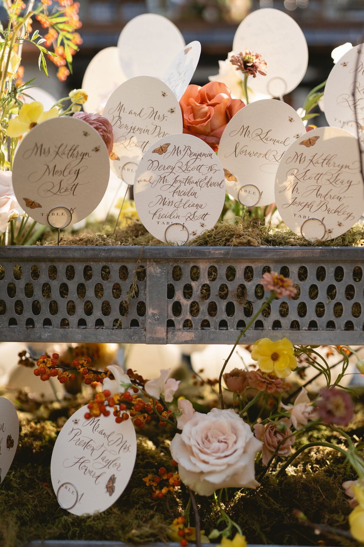 Unique floral planter escort display for fall wedding at private residence. Moss filled planters with floral such as ranunculus, butterfly ranunculus, roses, zinnias, and bittersweet popping out to create organic floral design for fall wedding reception escort display. Design by Rosemary & Finch Floral Design in Nashville, TN.