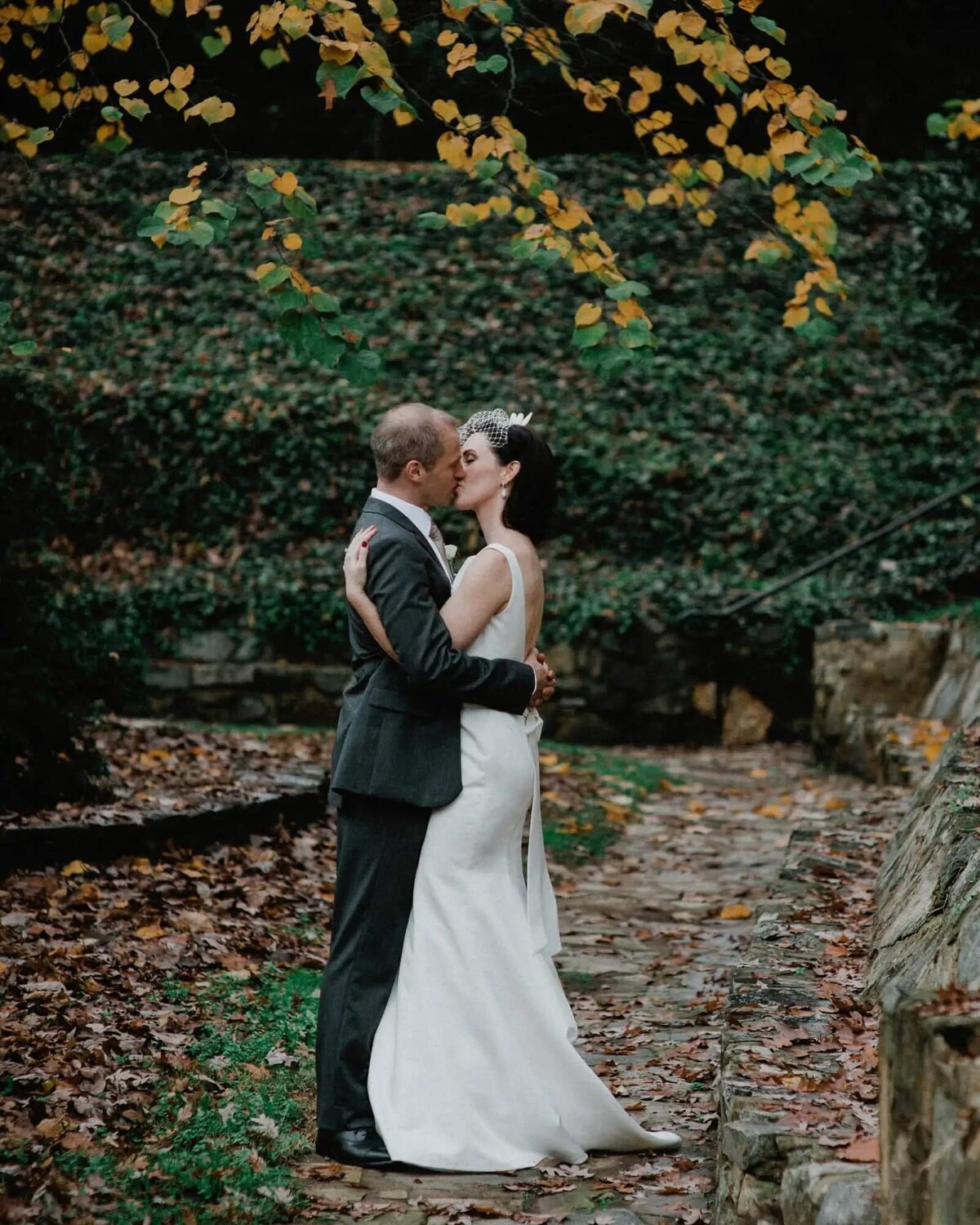 A bride and groom kissing on a leaf covered path.