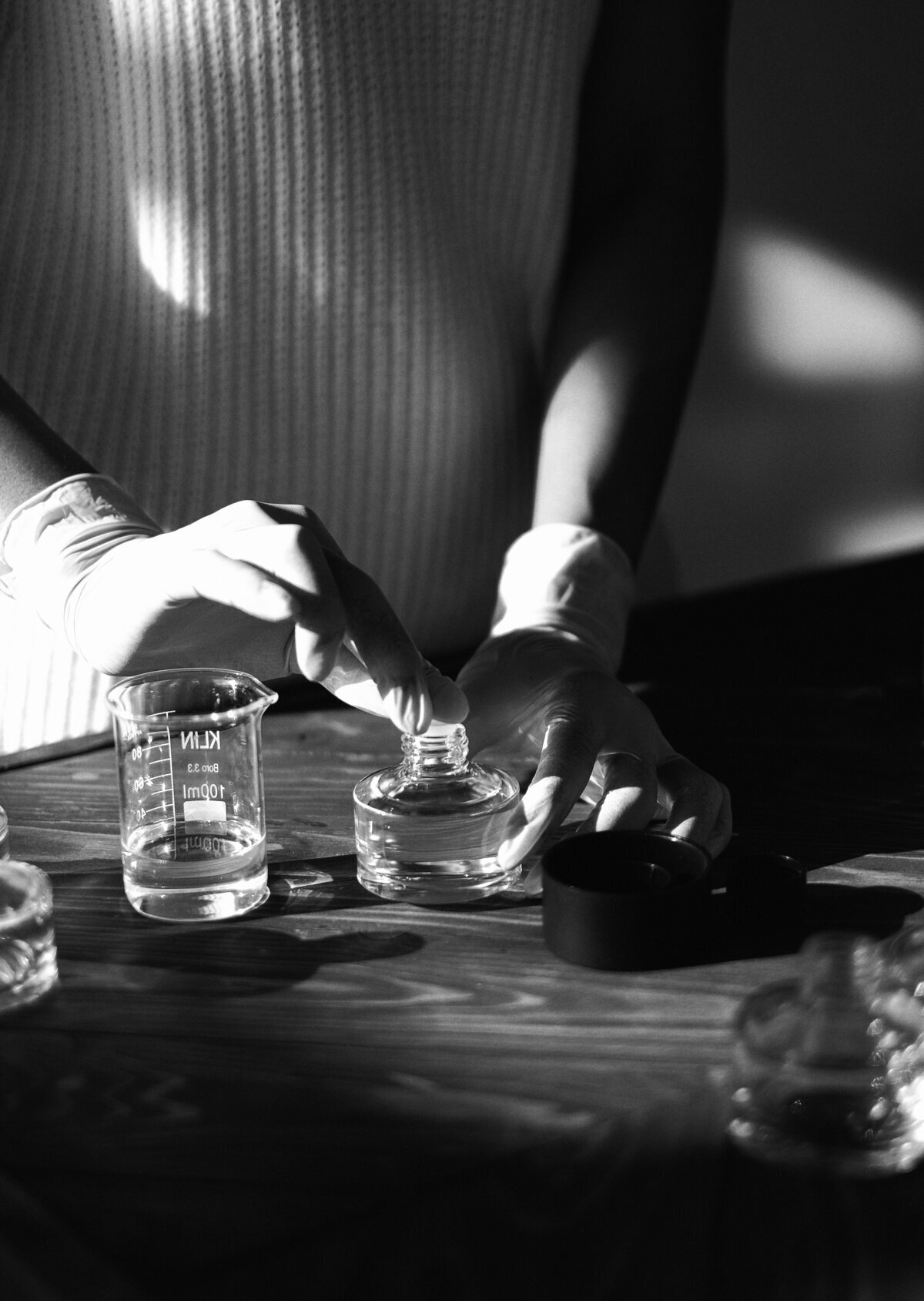 Mains portant des gants en caoutchouc et faisant de la chimie à l'aide d'ustensiles posés sur une table en bois.