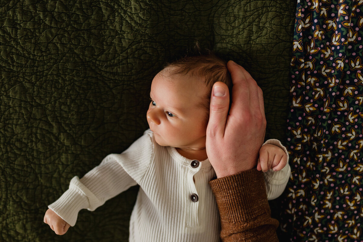 Baby laying on a bed with dad playing with hand.