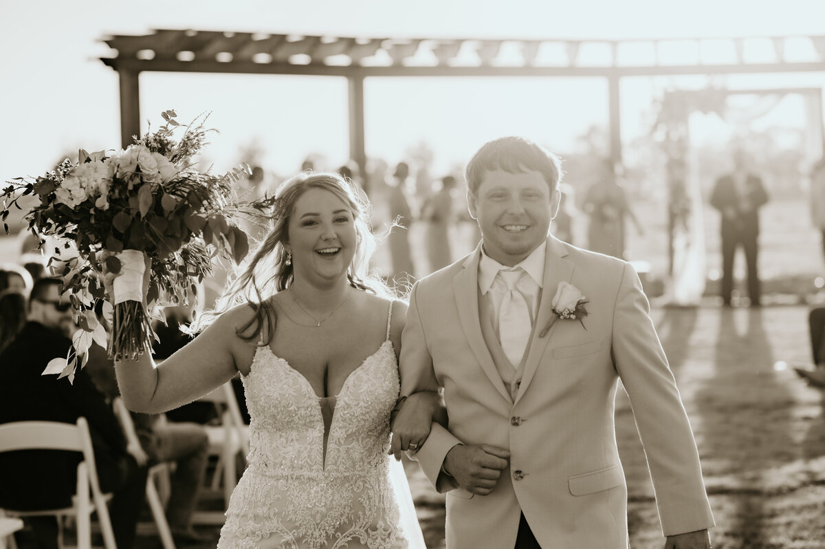bride and groom walking down the aisle together while the bride holds up her floral bouquet in the air captured by Best Little Rock wedding photographer