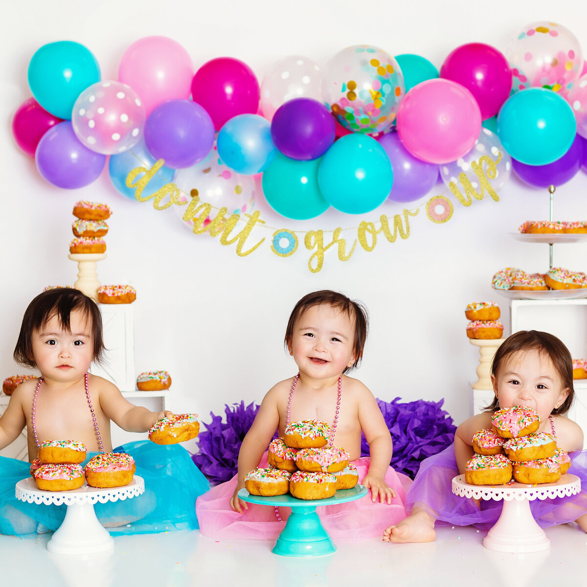 Family Photographer, three babies sit beside each other eating iced donuts