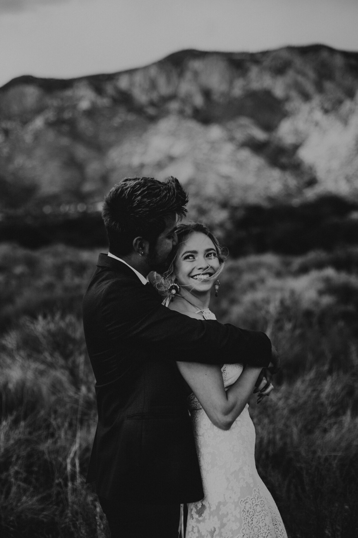 groom kissing bride in desert while she smiles