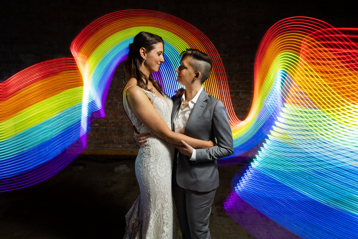 LGTBQ+ couple embracing on their wedding day in front of rainbow light painting