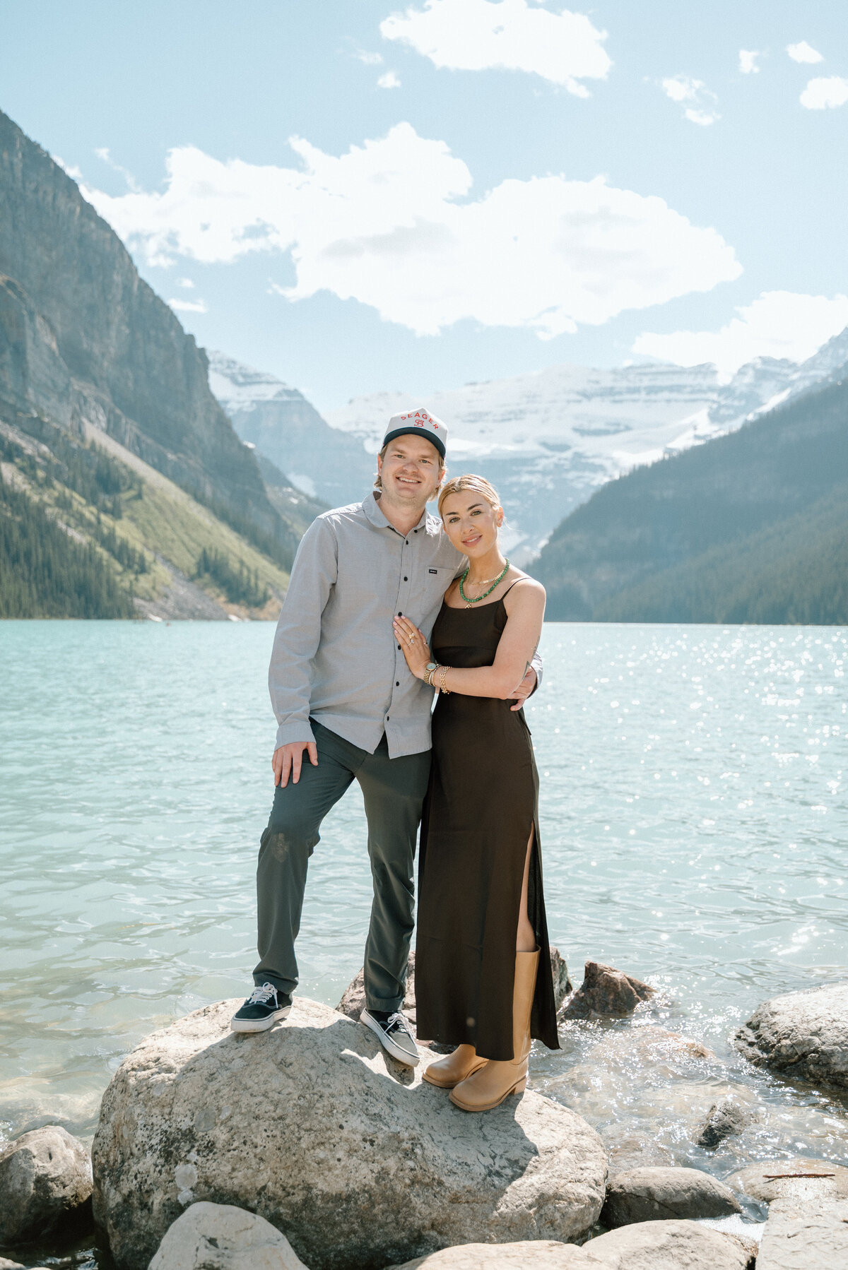 Casual engagement portraits on the rocky shore of Lake Louise with mountain views.