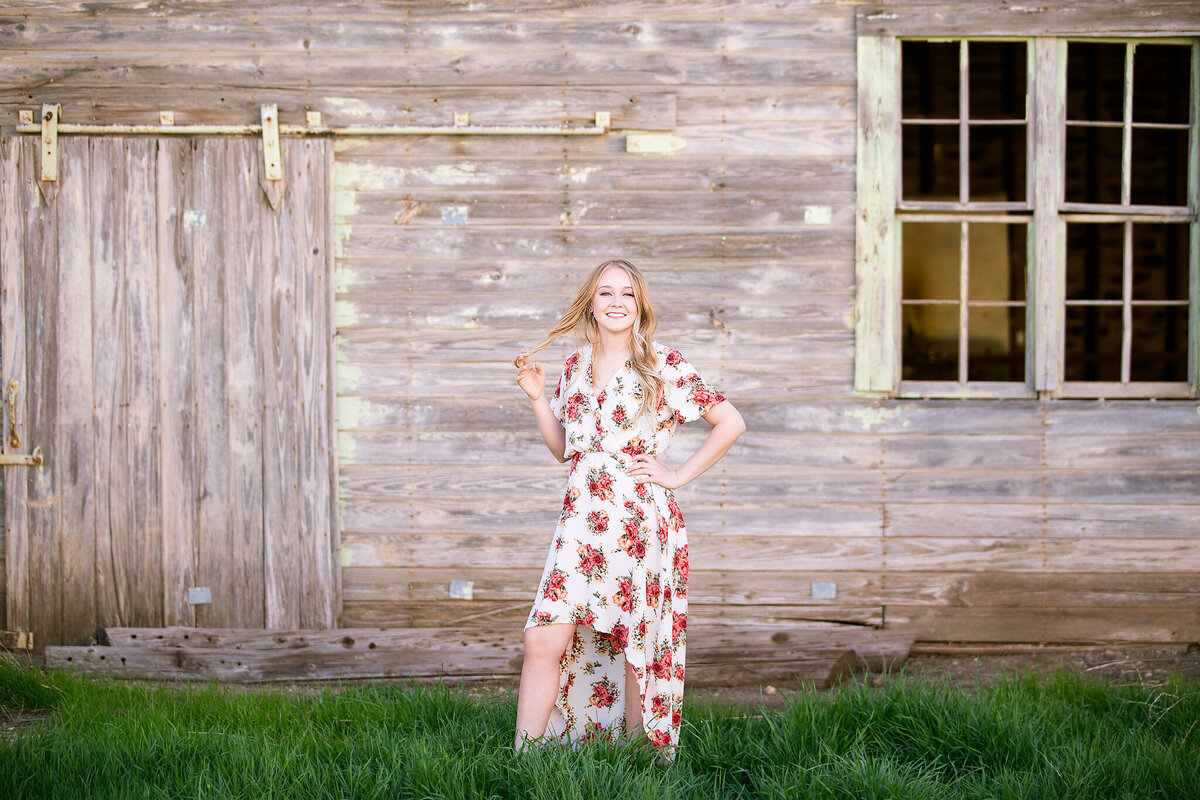 Girl in flower dress staning in green grass against barn in Happy tx