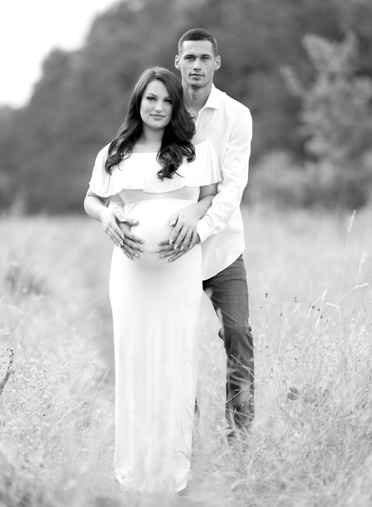 pregnant couple standing in a field dad holding belly