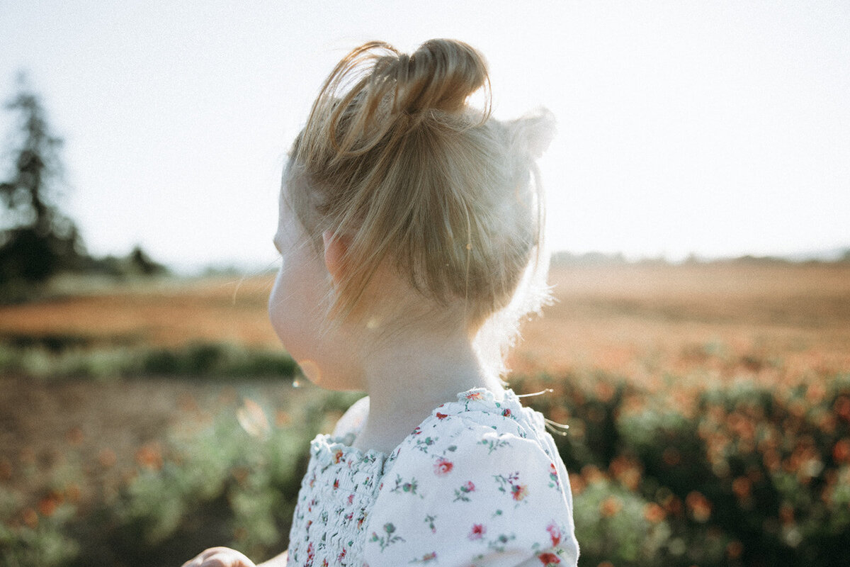 Toddler looks away as sunlight flows through her blond hair. 