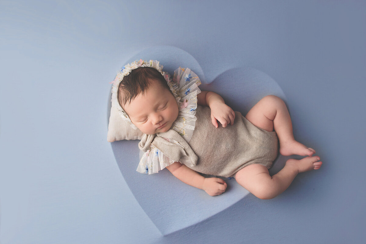 Newborn baby wearing floral bonnett and grey outfit laying in heart bowl during newborn photoshoot in Mount Juliet tennessee photography studio
