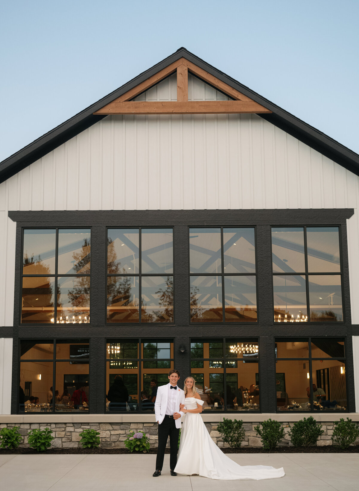 A bride and groom stand at golden hour in front of a building with large windows. 