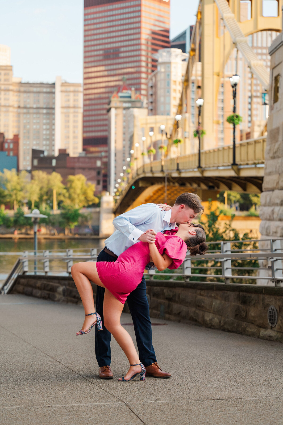 couple posing for photos after they got engaged with the pittsburgh yellow bridges behind them