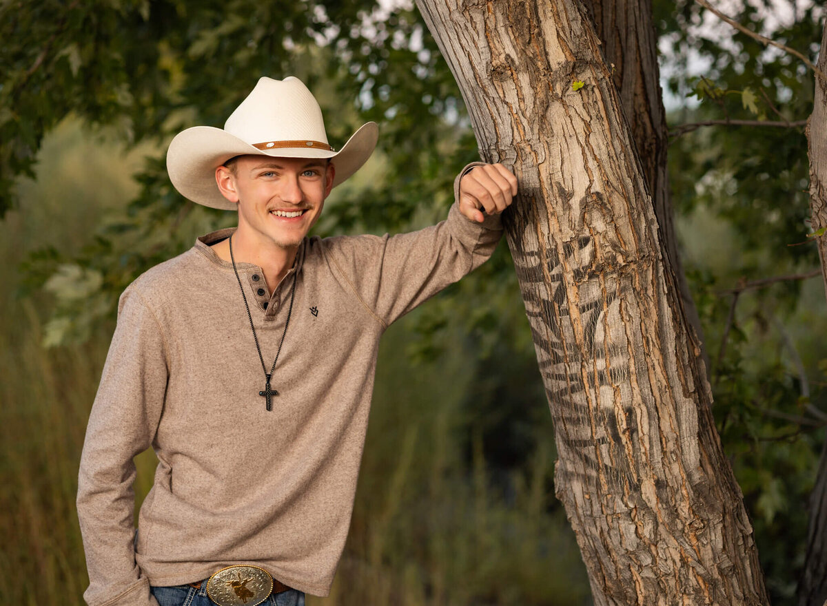 high school senior boy in white cowboy hat leaning against a tree