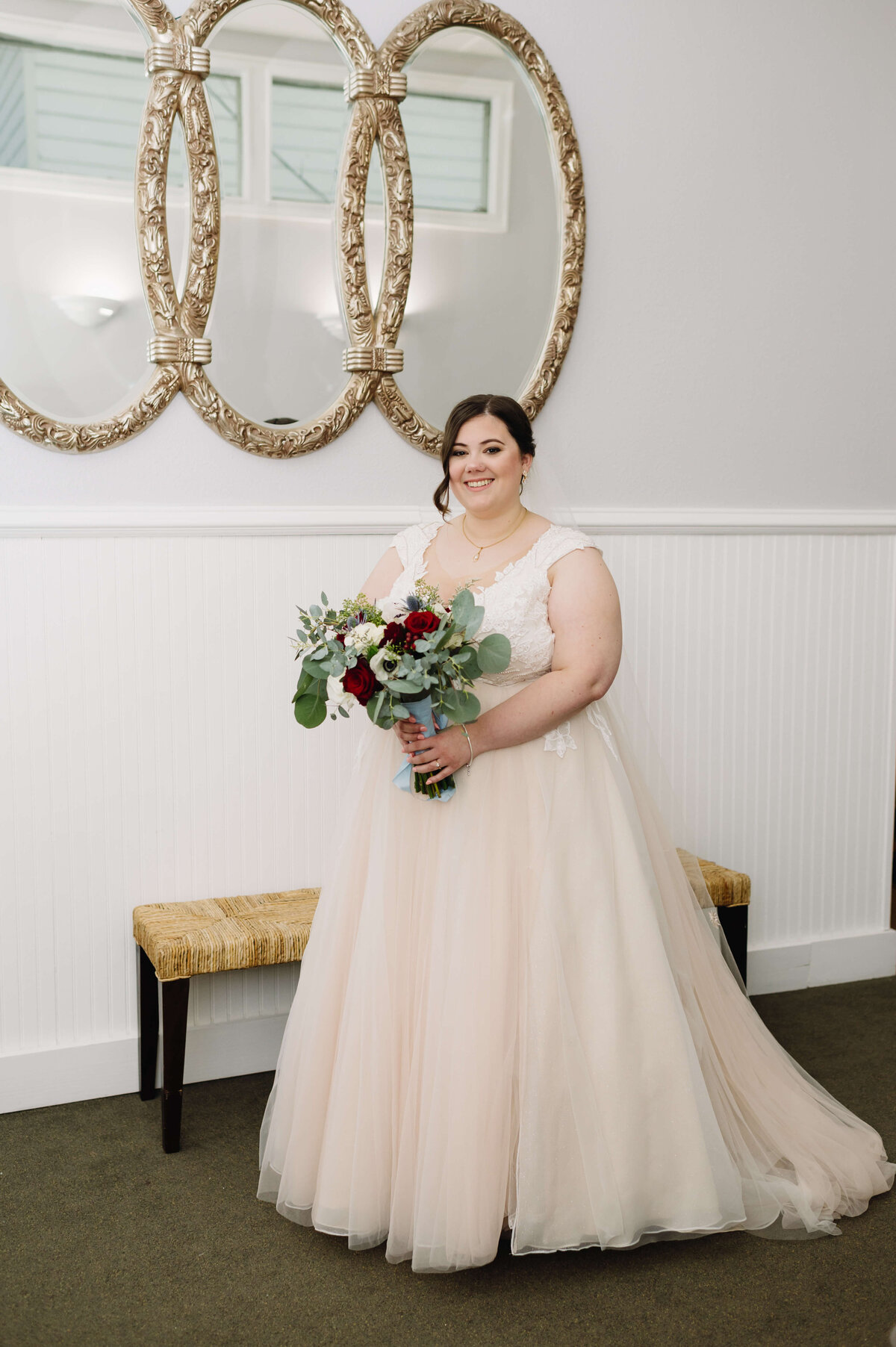 bride standing in front of a triple vintage mirror at Richmond wedding venues bridal suite holding her flowers and smiling