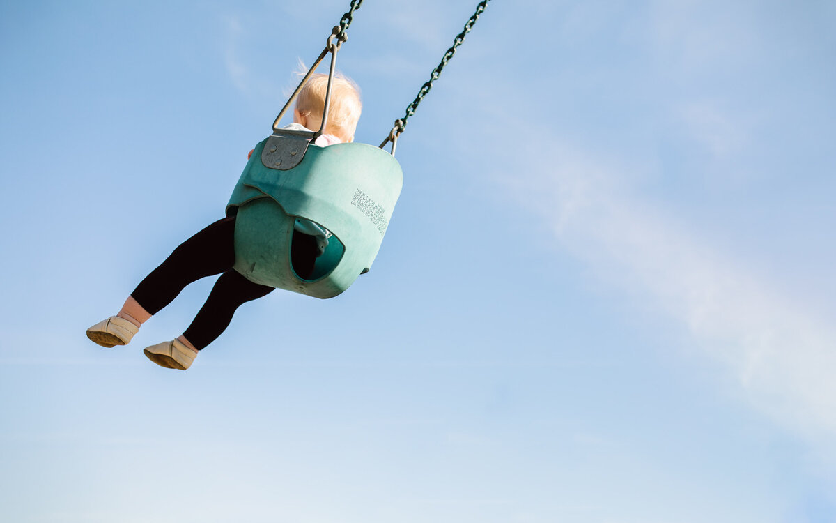 toddler girl swinging in blue sky