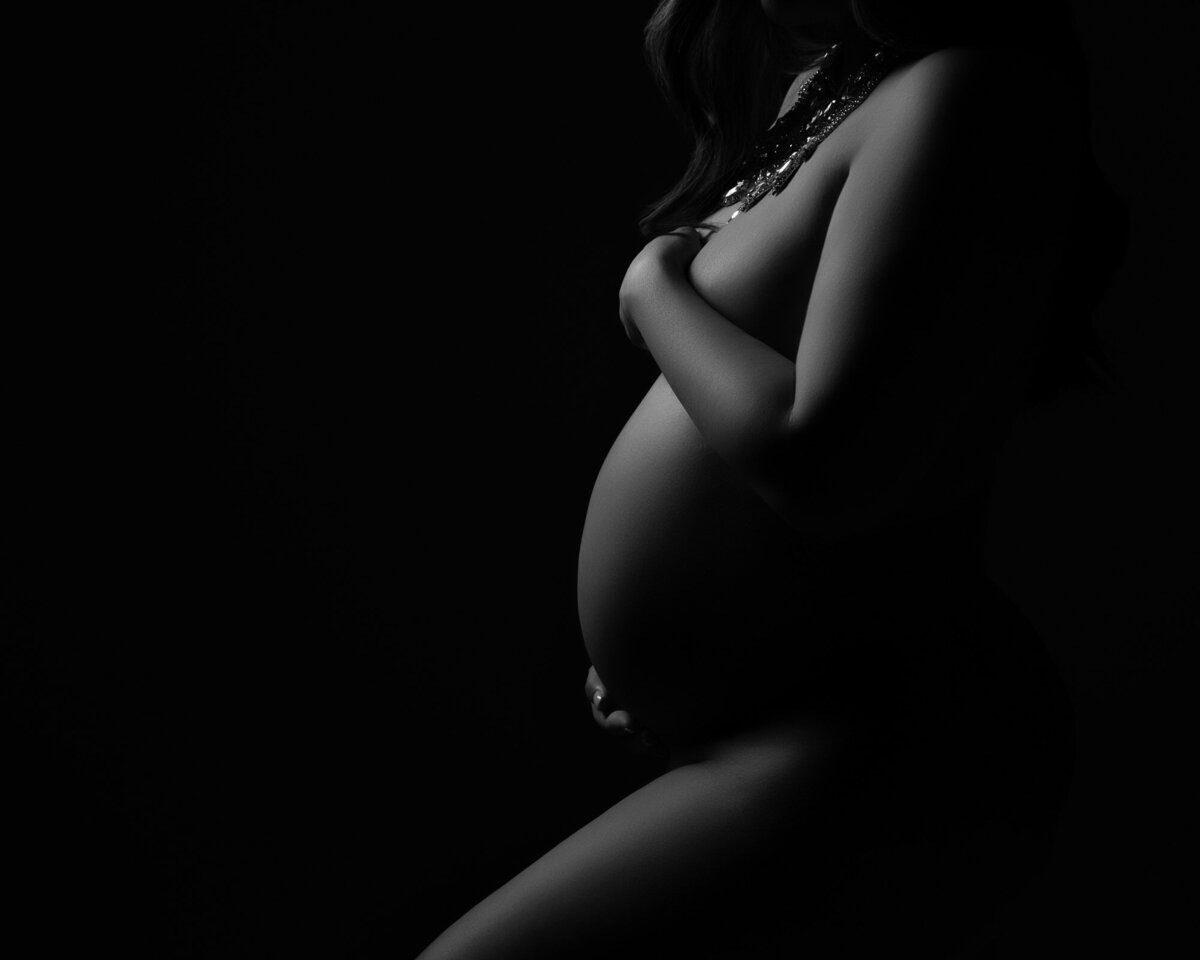 Fine art maternity photography featuring artistic nude study with dramatic studio lighting
