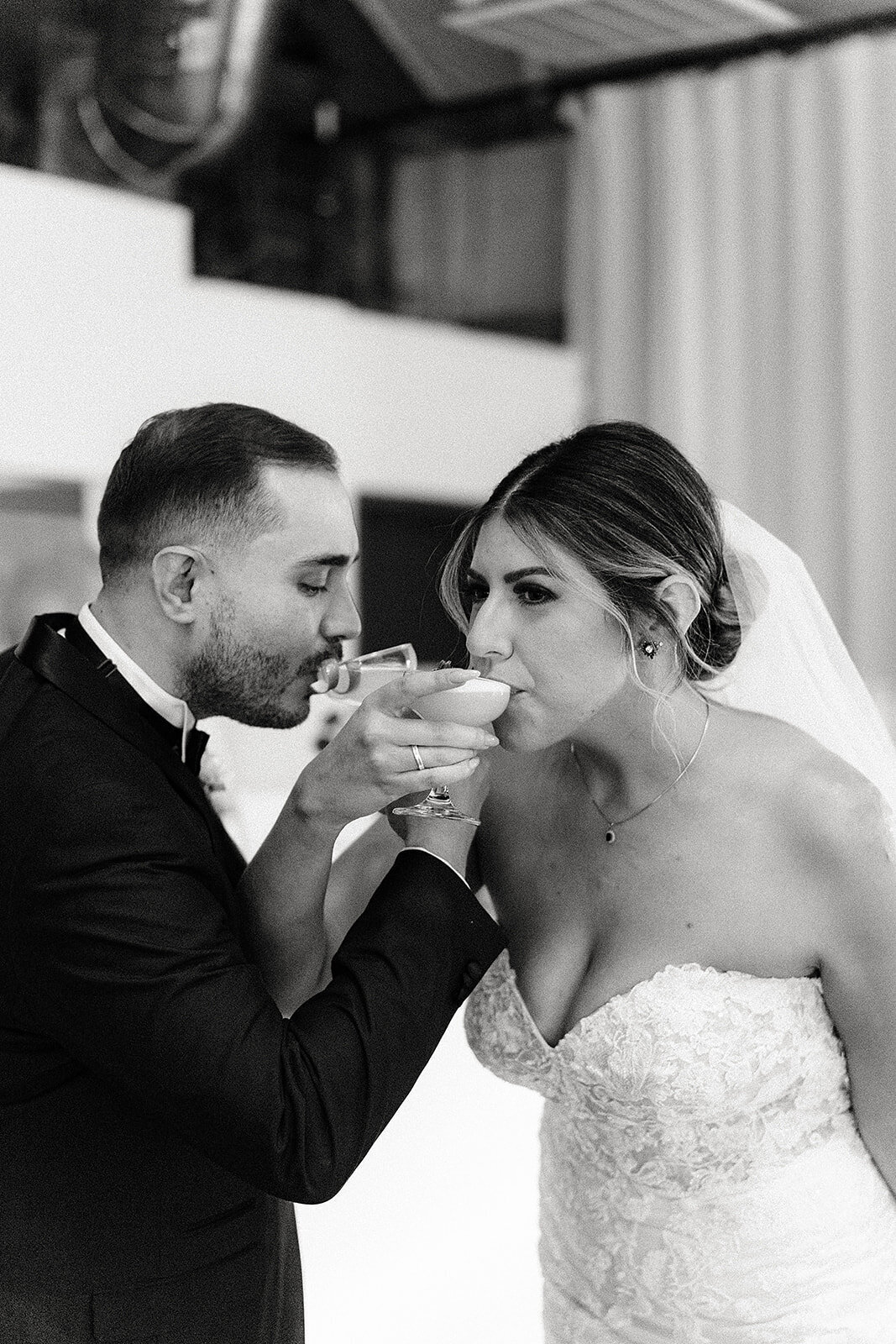 The bride and groom drink from their cocktail glasses together, sharing a quiet and happy moment after the ceremony, both dressed elegantly.