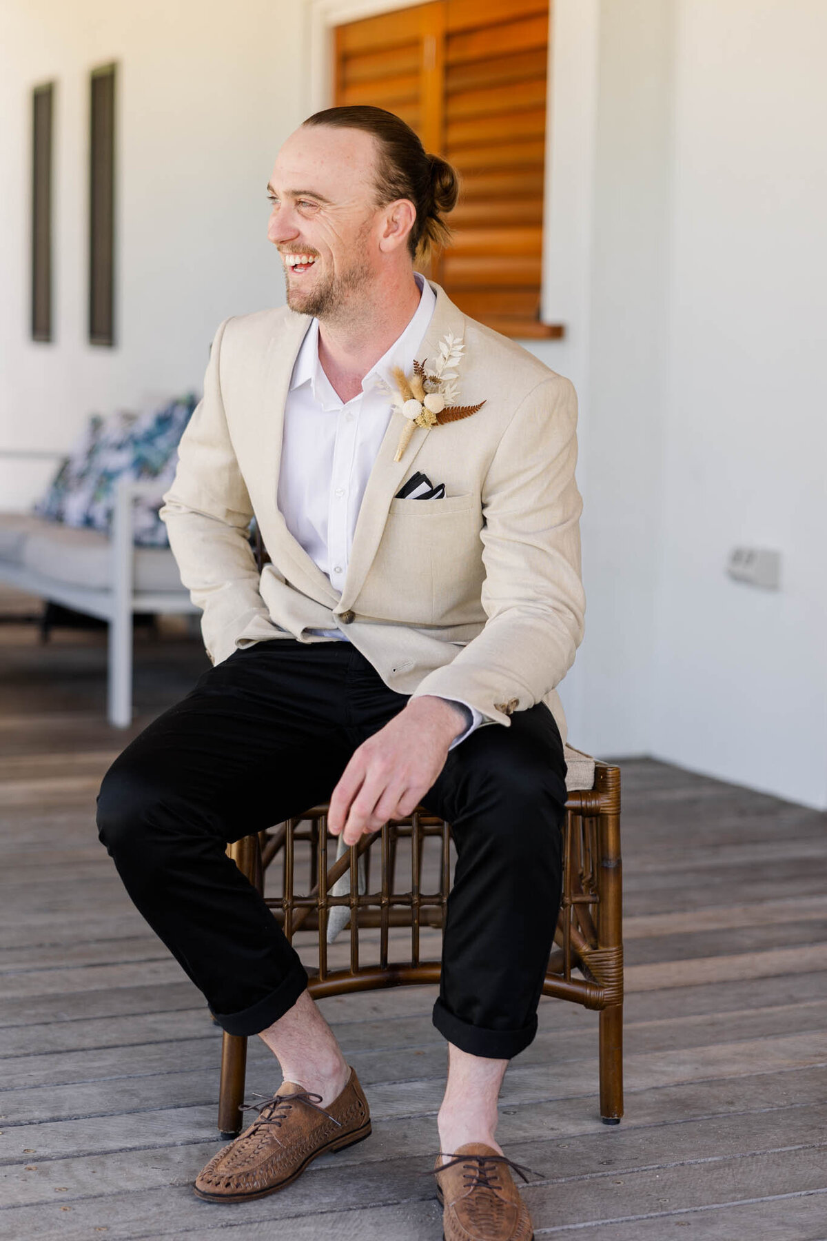 groom sits on a chair and laughs on his wedding day.
