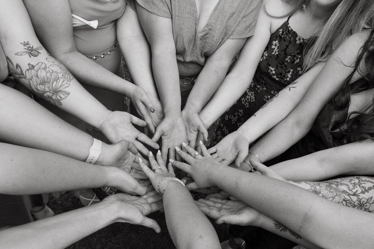 Friends of bride all bring their hands together  in a black and white photograph.