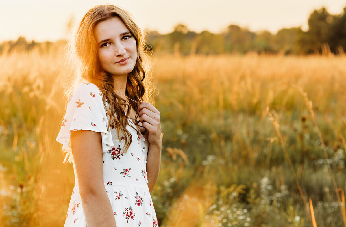 stunning senior posing in a field at sunset during her senior session