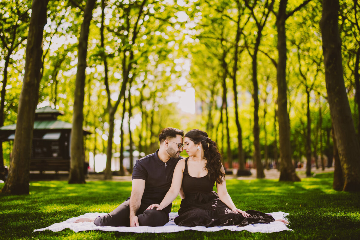 An engaged couple share a moment while sitting on the grass at pier A park in hoboken nj
