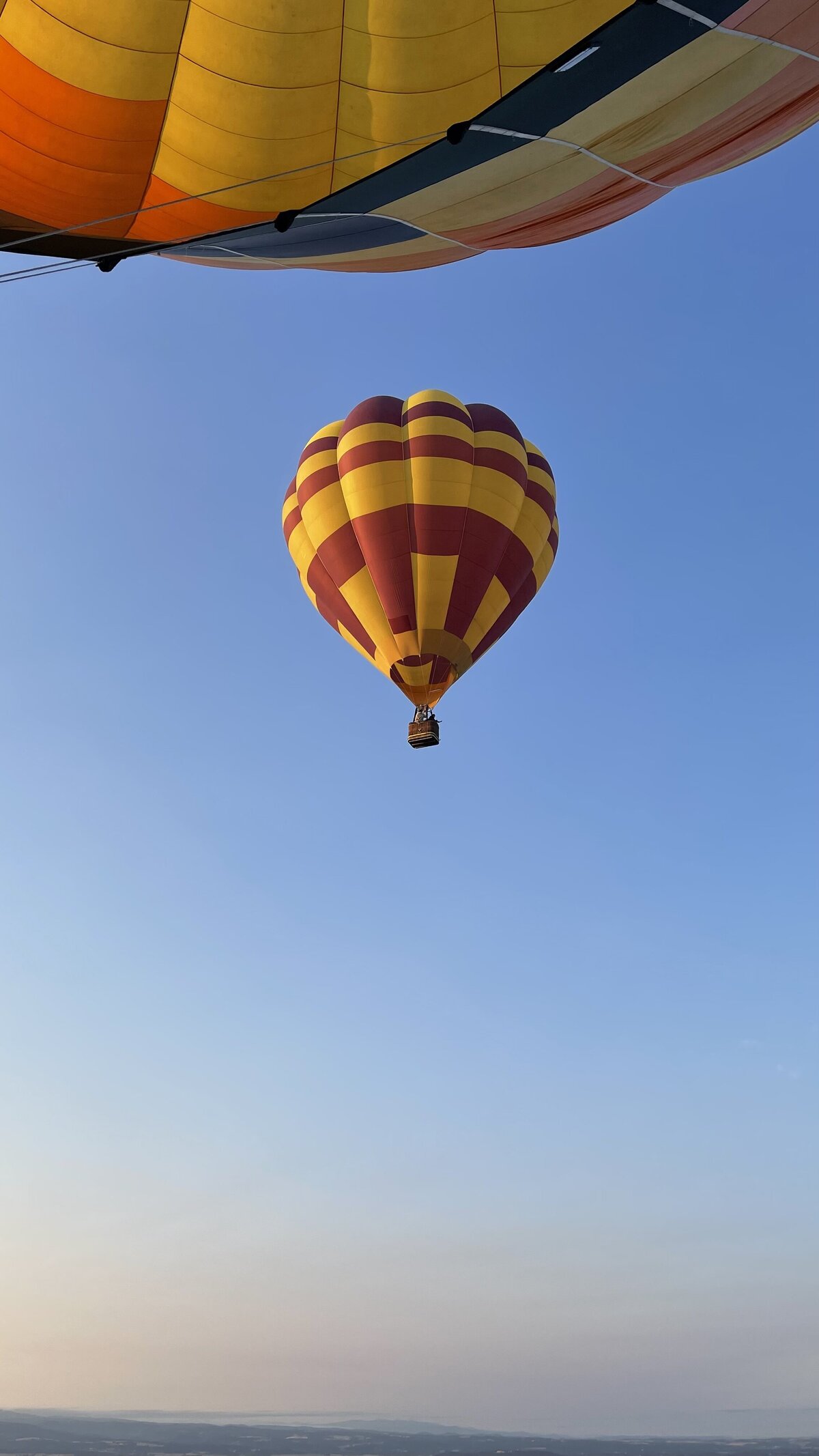 From inside a hot air-balloon in the sky, another red, and orange hot air balloon.