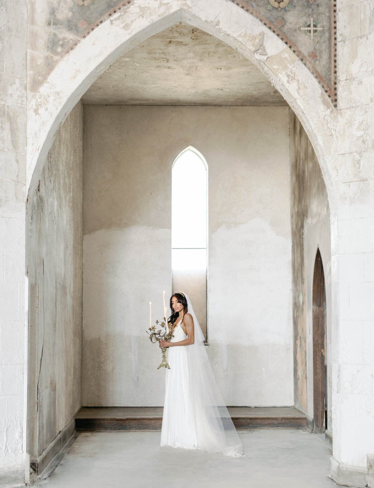bride with candelabra under crumbling arch in beautiful abandoned cathedral, ruins wedding venue in Europe