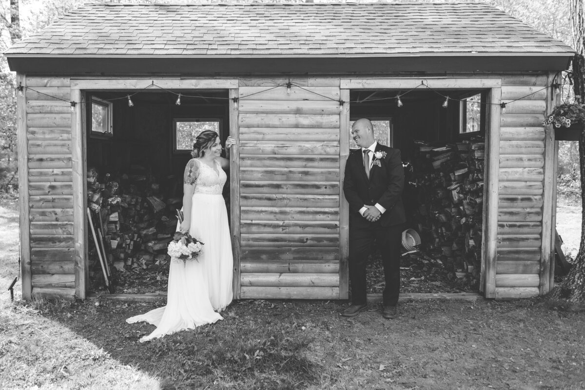 Black and white photo of bride and groom on wedding day near wood shed