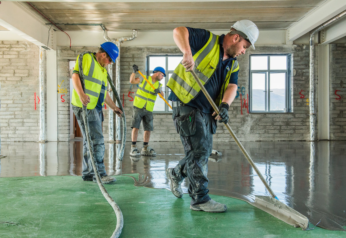 Builders laying liquid concrete floor in building
