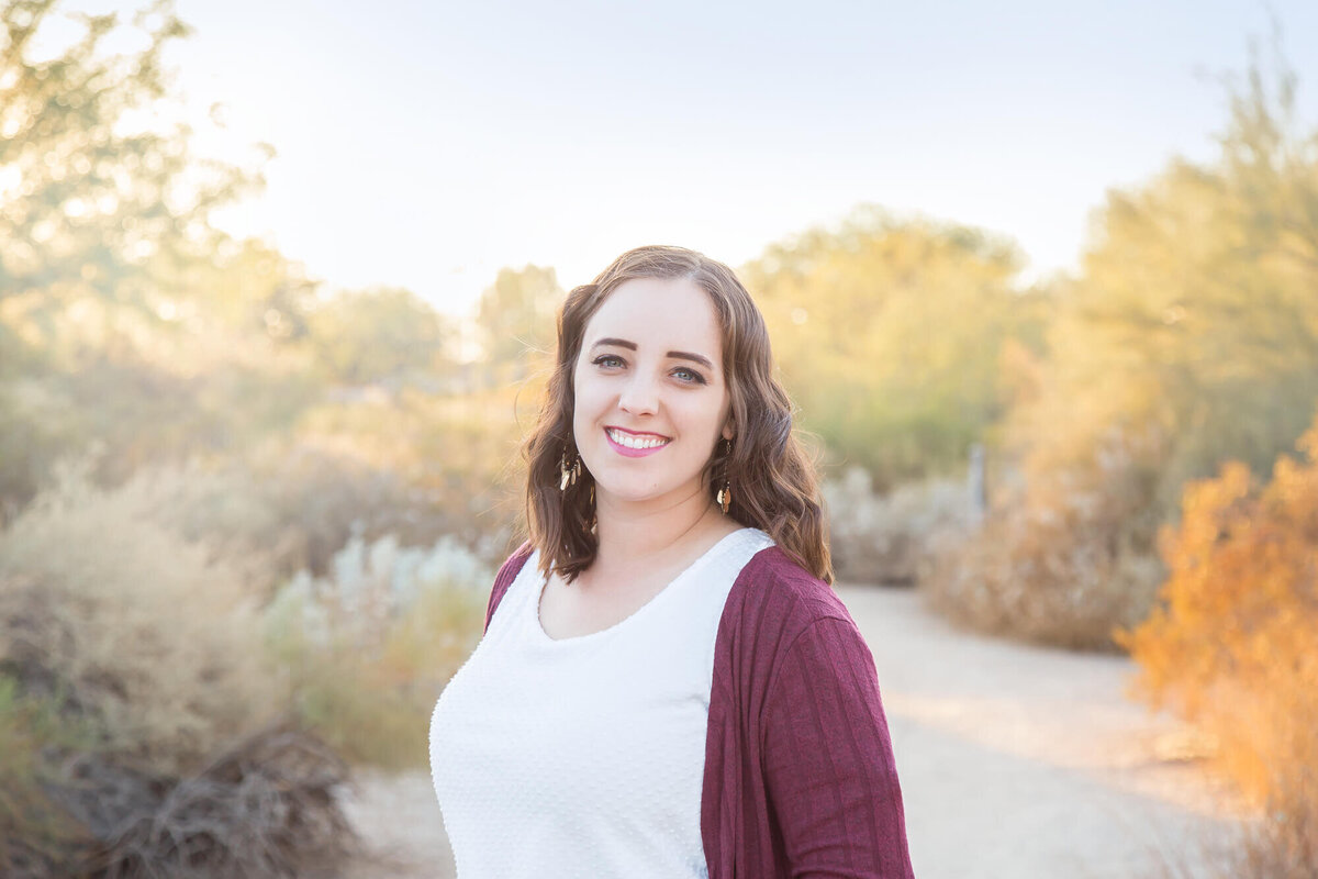 brown haired woman in white shirt with maroon sweater smiling on a desert path in Arizona