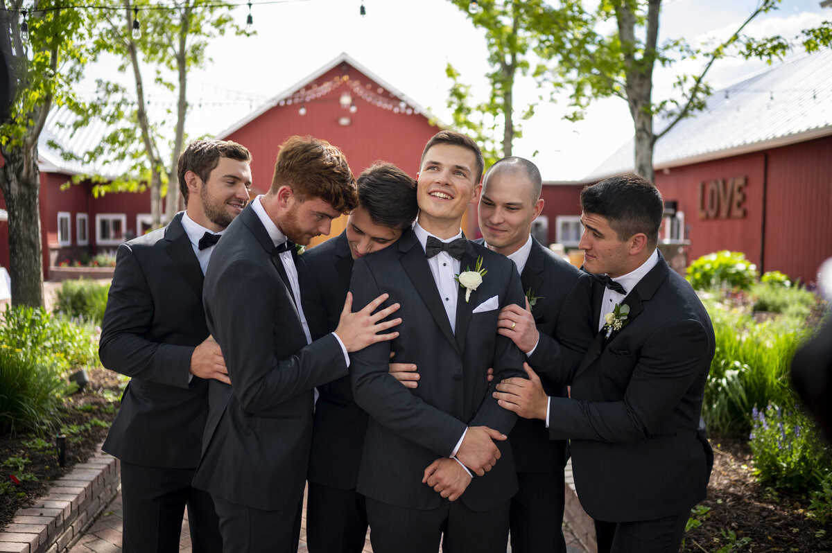 Groomsmen jokingly cuddling with Groom in front of wedding venue