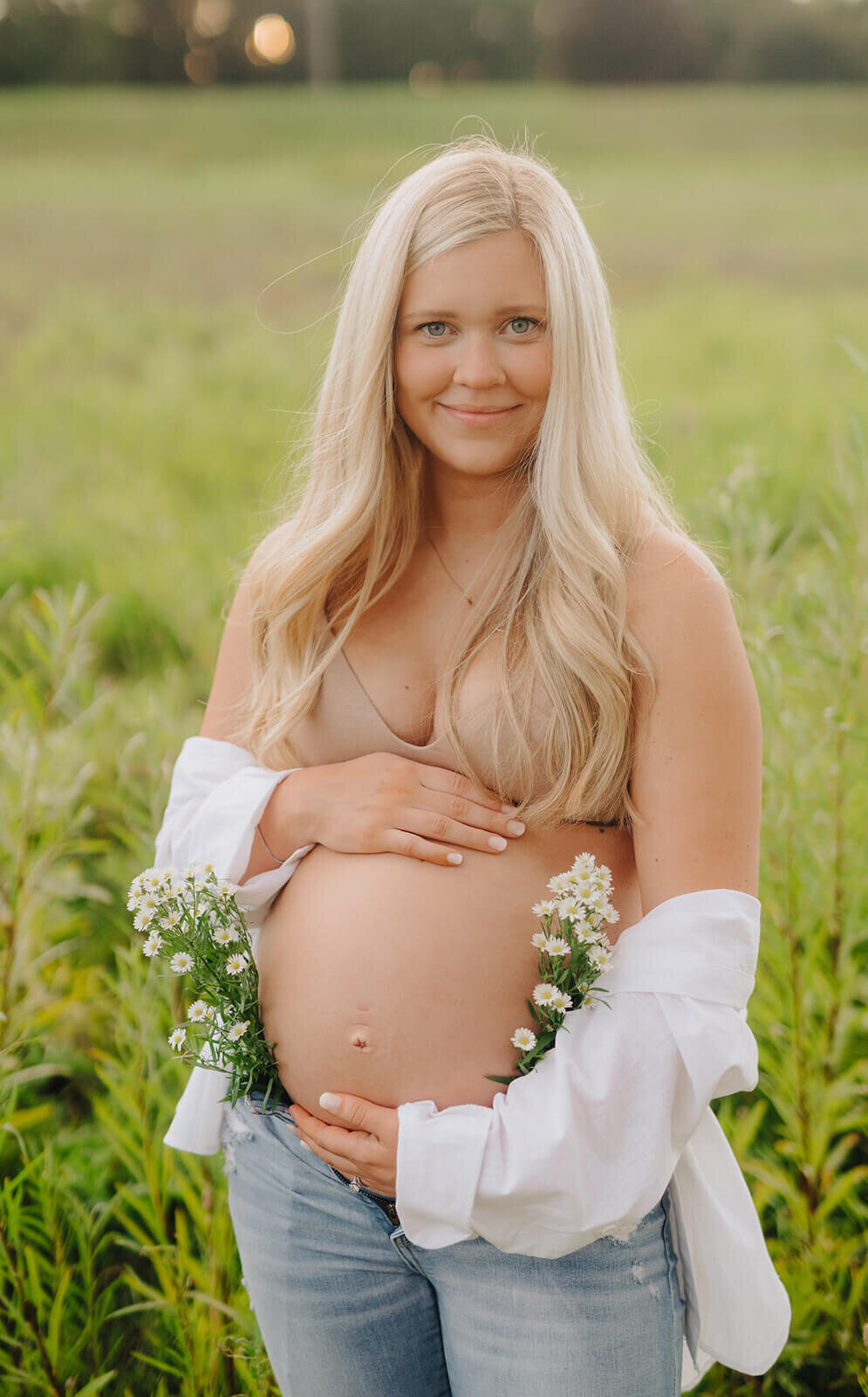 woman holding bare baby bump with florals surrounding her