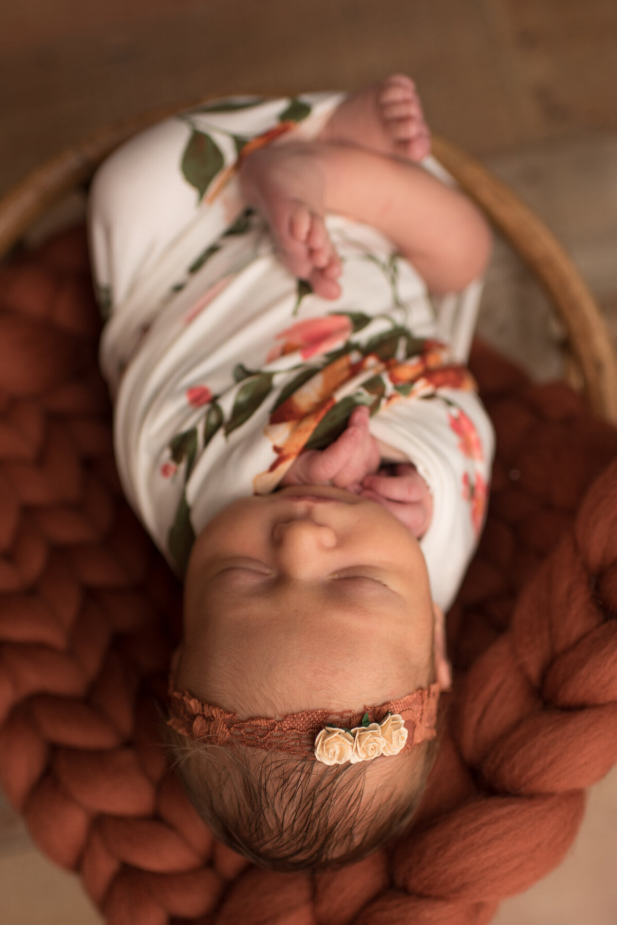 Baby girl wrapped in floral wrap with orange headband and basket