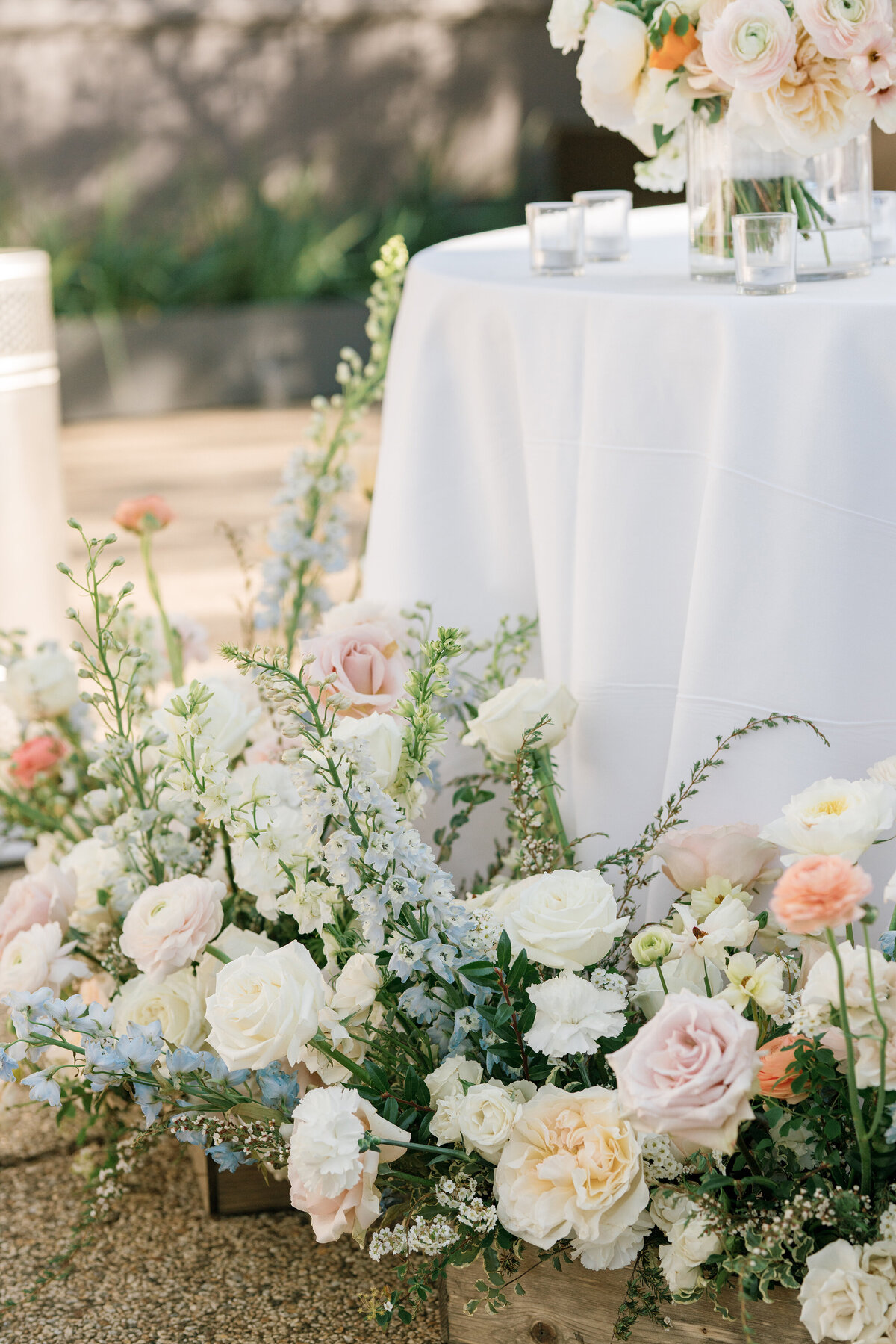 Light pastel roses and bluebells in wooden garden planters in front of head table at wedding reception