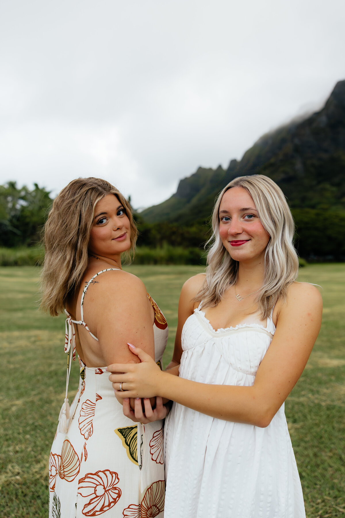 Two best friends posing together in flowy dresses during a photoshoot surrounded by the mountains of Oahu.