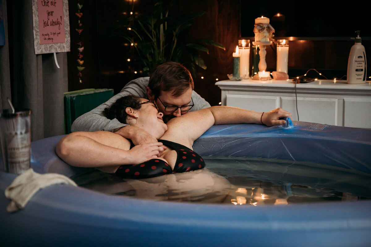 man kissing wife while she sits in birth pool
