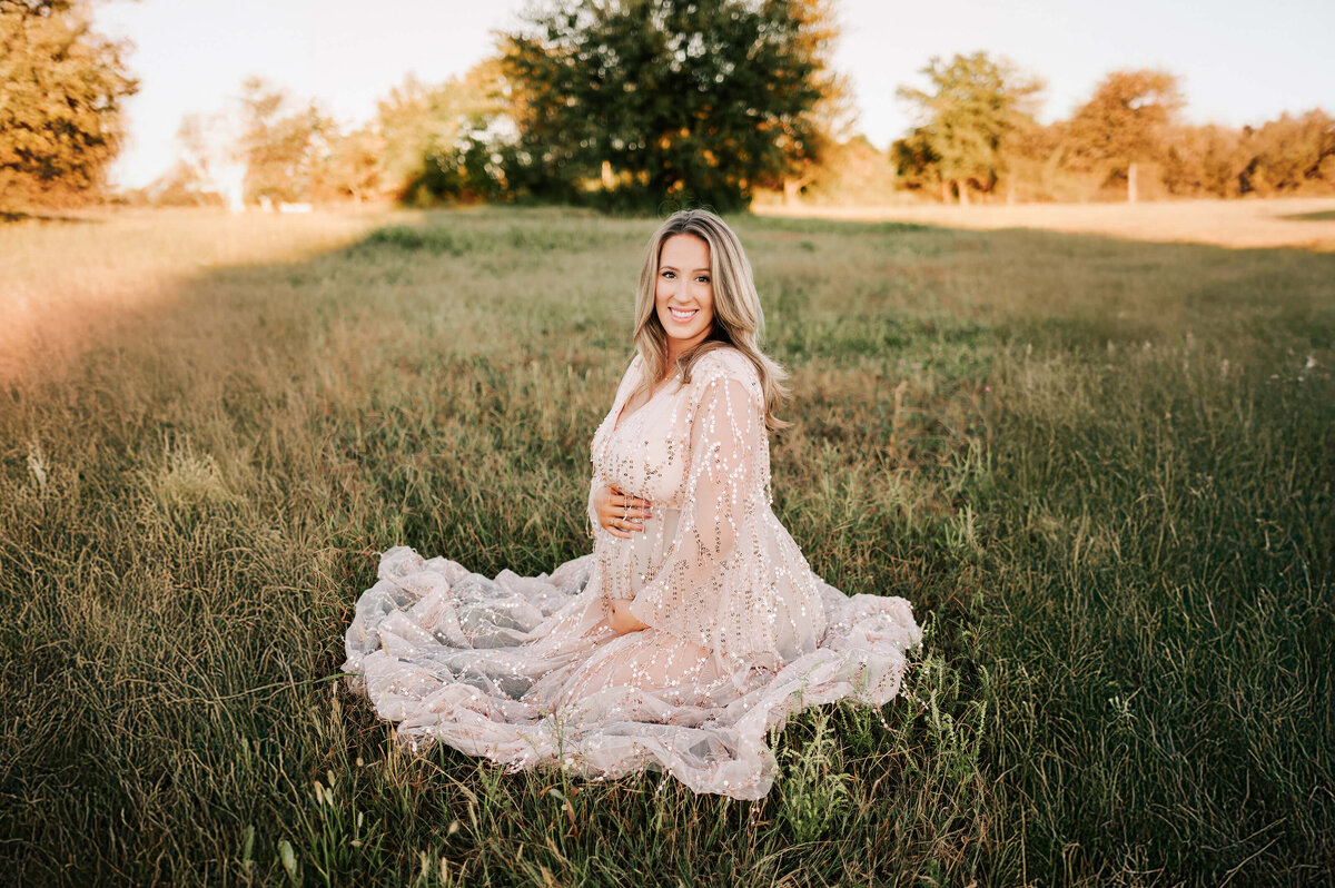 pregnant mom kneeling in field in Springfield MO during maternity pictures