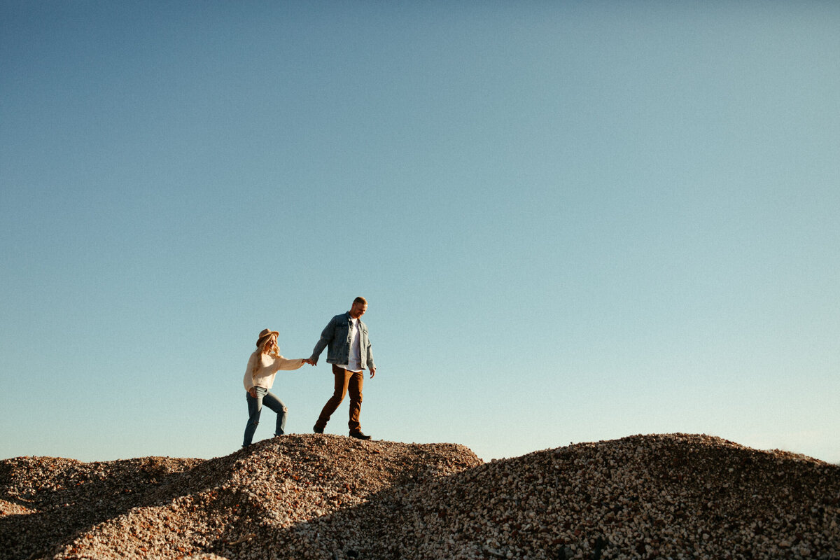 Adventurous couple holding hands and walking along the top of a rocky hill