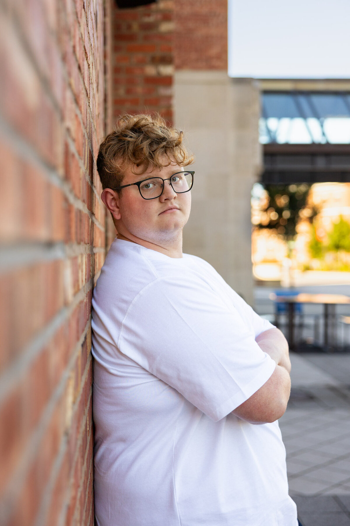 A senior guy leaning up against a brick wall looking at the camera from the side in Lawrence, KS