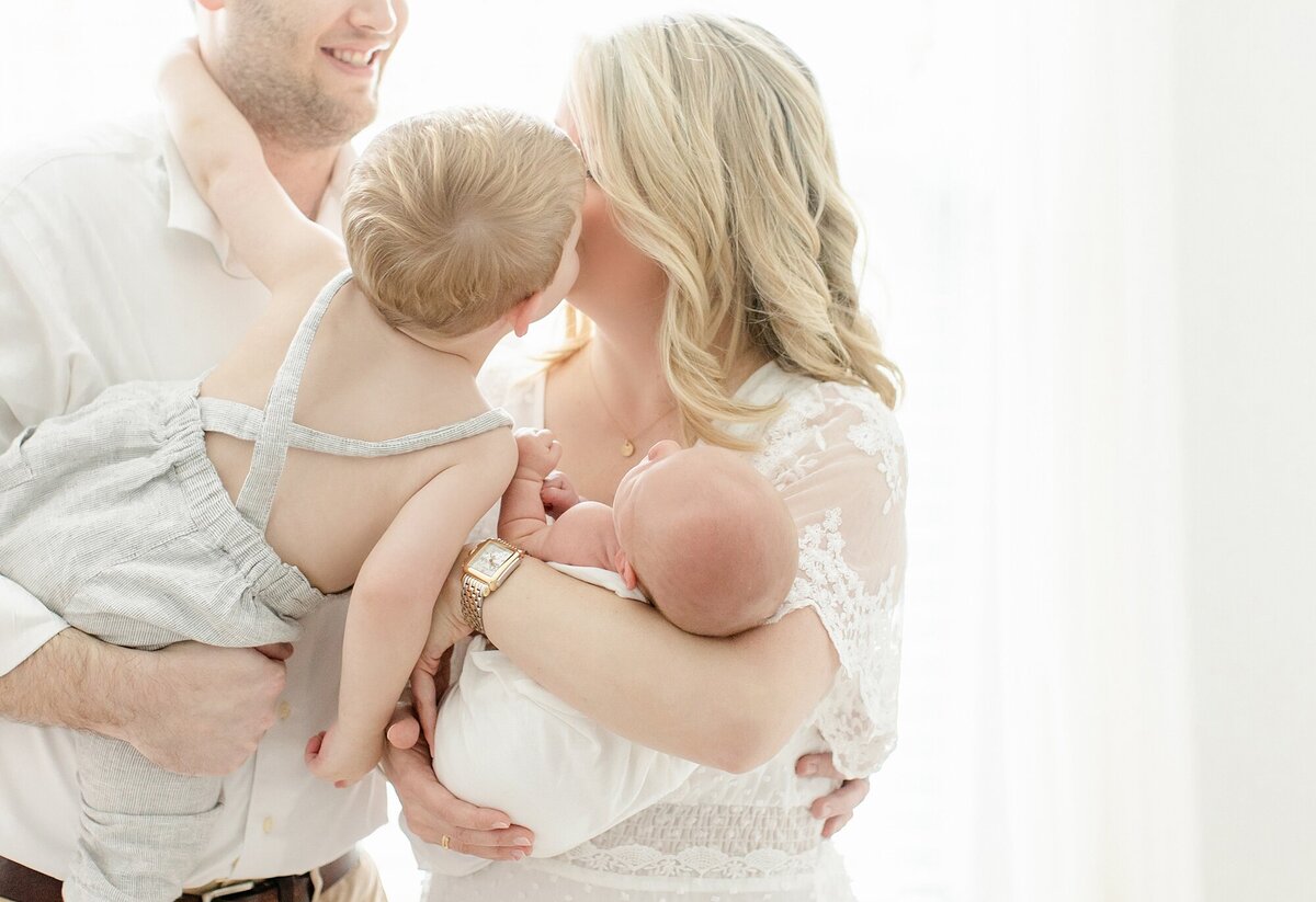 little boy kissing mom who is holding newborn