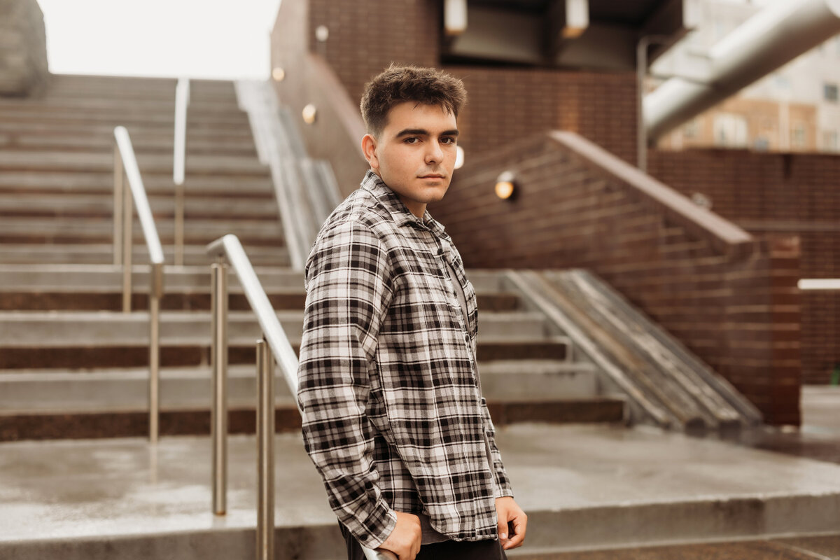 high school senior boy leans against metal stair rail downtown for his urban high school photos