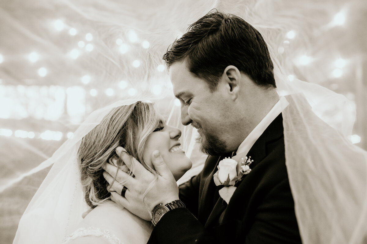 bride and groom standing under the bride veil as the groom holds the brides face and they smile at each other captured by little rock ar wedding photographer