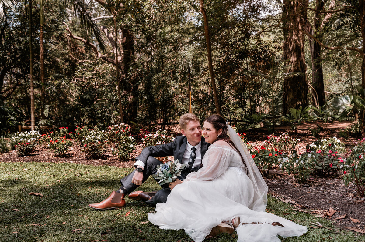 bride and groom sitting in the garden with husband looking at wife with love - Townsville Wedding Photography by Jamie Simmons